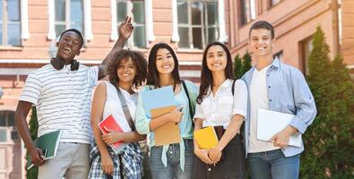 Group of happy students posing outdoors after lecture in university, resting between classes, looking at camera and smiling, free space photo