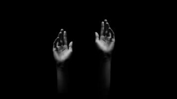This image features two hands reaching upward, with fingers extended, against a dark, black background. The hands are the main focus of the image, and the darkness adds a sense of mystery photo
