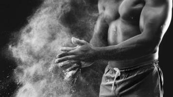 A man claps his hands, creating a cloud of chalk dust, against a black background. photo