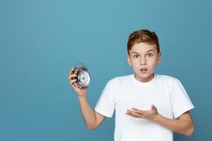 Image portrays a teen boy holding an alarm clock with a surprised expression, isolated on a blue background, suggesting urgency photo
