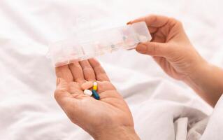 Cropped of woman holding a white pill bottle in one hand and a handful of assorted pills in the other hand, appears to be examining the pills closely, possibly preparing to take or organize them. photo