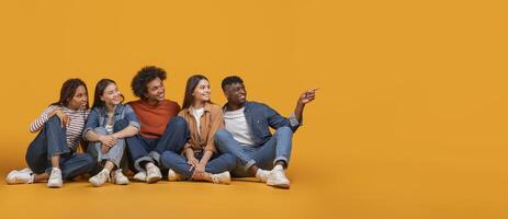 Five young adults, a diverse group of friends, are sitting on a yellow background. They are all smiling and looking to their right, with one person pointing towards the empty space photo