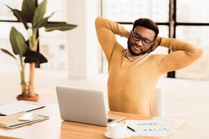 Time For Break. Successful black stock trader in glasses stretching hands at workplace, free space photo