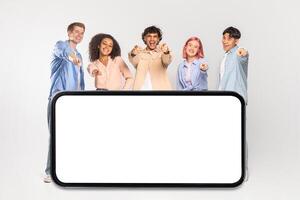 A diverse group of five young adults, each with unique hairstyles and fashion choices, stand in front of a large smartphone with a blank white screen. photo