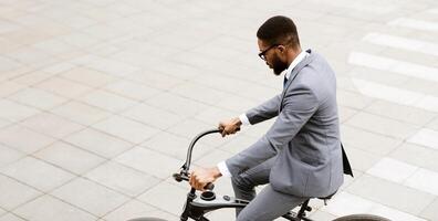 An executive black guy is commuting by bicycle in a cityscape. The mood is energetic and productive, with a focus on a healthy and efficient mode of transportation. photo