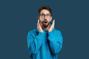 A man wearing glasses with a surprised expression on his face. His eyes widen, eyebrows raise, and mouth forms an O shape in astonishment. The man appears shocked or startled by something unexpected. photo