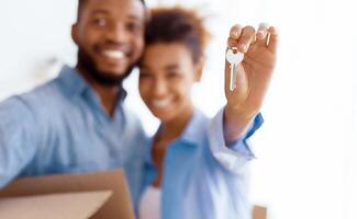 New Home. Happy Afro Couple Showing Keys Embracing After Moving In Own House Standing Indoor. Selective Focus, Shallow Depth photo