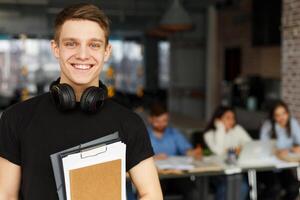 Handsome male student posing in campus library with classmates on background, free space photo