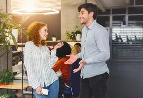 A man and a woman are standing next to each other in a professional office setting. They appear to be engaged in a conversation or discussing work-related matters. photo
