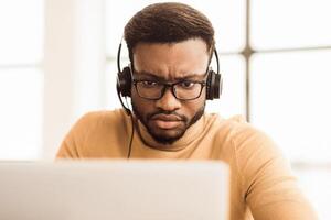 Helpline Concept. Focused african call center agent consulting client looking at laptop. Empty space photo