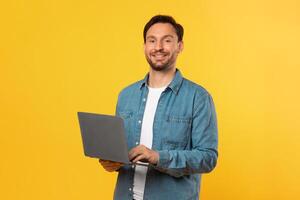 A man wearing a blue shirt is shown holding a laptop with both hands. The man appears focused on the screen of the laptop, possibly working or browsing photo