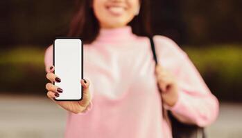 A woman is holding a cell phone in her hand, looking at the screen with a focused expression. She appears to be scrolling or texting, engaged with the device, cropped photo
