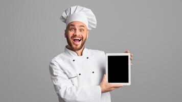 Professional Chef Showing Tablet Computer Blank Screen Recommending Food Delivery Application Or Online Menu Over Black Background. Studio Shot, Mockup photo