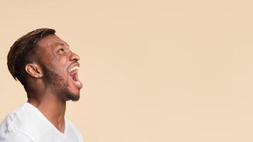 Anger. Aggressive Black Guy Screaming Loudly Standing Over Yellow Background In Studio. Panorama, Copy Space, Side View photo