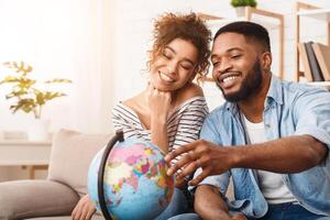 African American man and woman are sitting comfortably on a couch, attentively examining a globe placed between them. They seem engrossed in studying the geography displayed on the globe. photo