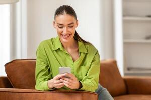 A woman is seated on a couch, engrossed in her cell phone. She appears focused as she interacts with the device, possibly texting or browsing social media. photo