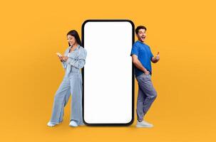 A man and woman are standing next to a blank screen on a bright yellow background. They appear to be discussing or presenting something, with a focused expression on their faces. photo