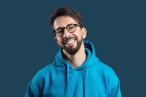 Man exudes a cheerful demeanor, showcasing a bright smile. He is dressed in a vibrant blue hoodie, adding a pop of color to the simple yet captivating backdrop. photo