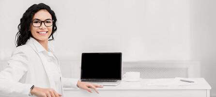 Online Course, Workshop. Happy mexican woman smiling at camera near computer with blank screen, mock up, copyspace photo
