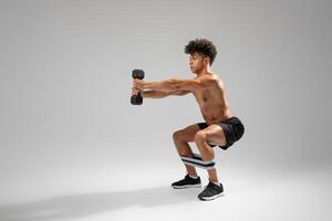 A young man engages in a strength training exercise involving weighted squats while using a dumbbell. He focuses on maintaining proper form as he balances on his feet with a resistance band photo