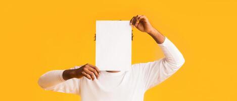 African american guy covering his face with empty white paper like mask, try to hide his real emotion, copy space photo