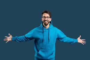 A man wearing a blue hoodie stands with his hands extended outward. He appears to be gesturing or reaching for something, with a focused expression on his face. photo