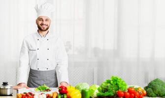 Male Chef In Uniform Smiling To Camera Standing Posing In Kitchen. Professional Cook Man Portrait. Selective Focus photo