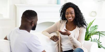 A woman sits on a couch and talks to a man, smiling and gesturing with her hands. photo