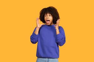 A guy with curly hair displays a surprised expression while raising his hands in a dramatic gesture. The yellow background adds a cheerful atmosphere, enhancing the emotional impact of the moment photo