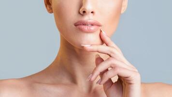 This image is a close-up shot of a woman face and hand. Her hand is resting on her chin, and her lips are slightly parted. The background is a light blue color, cropped photo