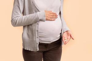 Medicines During Pregnancy. Unrecognizable Pregnant Woman Showing Pills In Hand Touching Belly Standing On White Background In Studio. Cropped photo