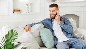 A man is seated on a couch, engaged in a conversation on his cell phone. photo