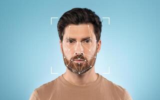 A man stands with a neutral expression while a facial recognition grid overlays his face, set against a solid blue background. photo