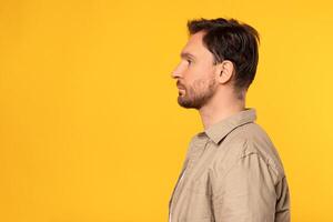 A man is standing in front of a bright yellow background. He is dressed casually and appears to be looking straight ahead, profile view photo