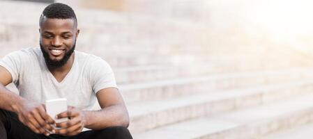 A man with a beard sits on a set of steps, looking down at his phone with a smile. photo