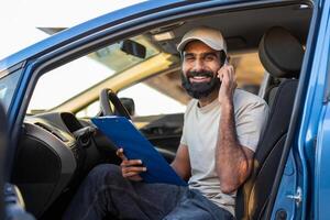 Indian man is seated in the drivers seat of a car, engaged in a phone conversation. He holds a cell phone to his ear, with a focused expression on his face photo