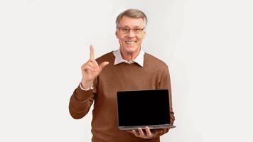 Great Offer. Smiling Senior Man Showing Laptop Blank Screen Pointing Finger Up Standing On White Studio Background. Panorama, Empty Space photo