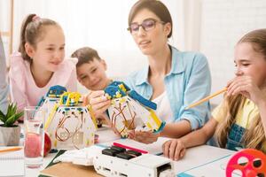 A group of young students are learning about robotics and engineering in a classroom setting. A teacher is helping them build and program a robot, while they work together and ask questions. photo