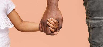 Cropped of adult males hand holding the hand of a little child. The hands are clasped together, showing a sense of connection and care. The image is set against a soft peach background photo