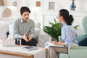 A man is engaged in a counseling session with a woman therapist in a comfortable living room. They are having an intense conversation, with the therapist taking notes photo