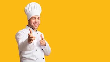 I Choose You. Cheerful Chef Man Pointing Fingers Winking At Camera Standing On Yellow Background. Studio Shot, Panorama photo