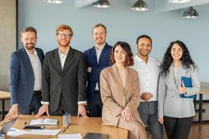 A group of diverse business professionals stand together in a modern office setting. They all look confident and successful, dressed in smart attire, and smiling warmly at the camera photo
