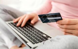 Cropped of woman sits at a desk, holding a credit card in one hand while typing on a laptop with the other hand, focused on entering information into the computer, shopping online photo