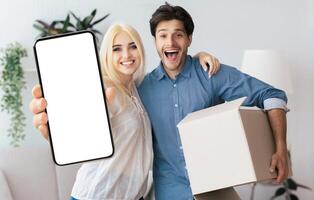 A happy couple smiles for the camera while holding a phone with a blank screen and a cardboard box. photo