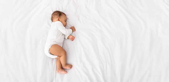 Angulo alto ver de bebé chico dormido en lado acostado en cama adentro. linda niñito niño descansando siesta durante tiempo de día dormir a hogar concepto. parte superior ver disparo. panorama con Copiar espacio foto