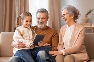 A family consisting of parents and children sitting together on a couch, engaged with a tablet device. They are focused on the screen, interacting with the content displayed. photo