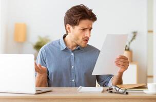 A man sits at a desk, looking confused and surprised as he reads a paper document. photo