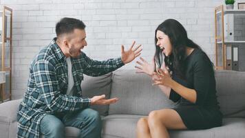 A couple is having a heated argument on a couch in their living room. The woman is sitting on the couch with her legs crossed and is gesturing wildly with her hands while yelling at the man. photo
