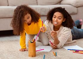 Black Mother And Little Daughter Sketching Together Playing And Bonding Lying On Floor Indoors. Selective Focus photo