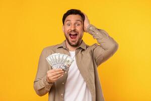 A man is seen holding money in his hand while making a comical expression on his face. His eyes are widened, and his mouth is twisted into a humorous smirk. photo